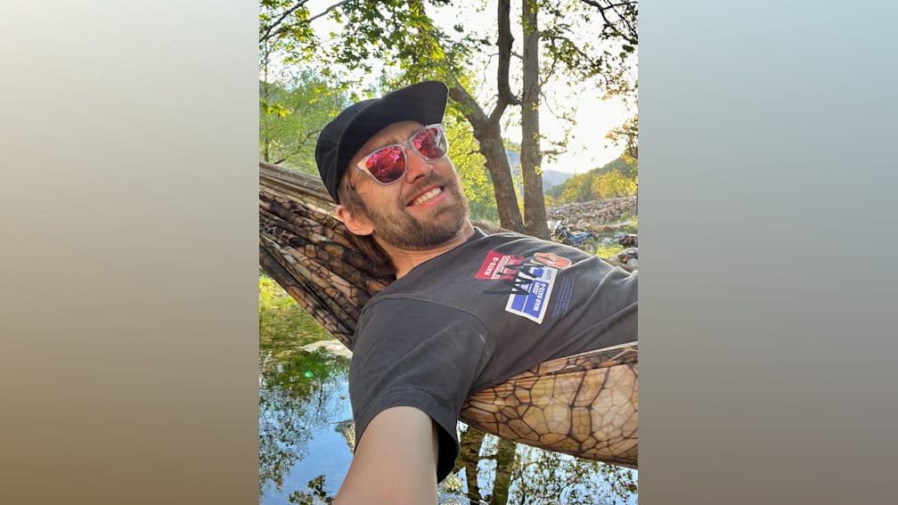 A man in a black shirt is lying in a hammock and taking a selfie.