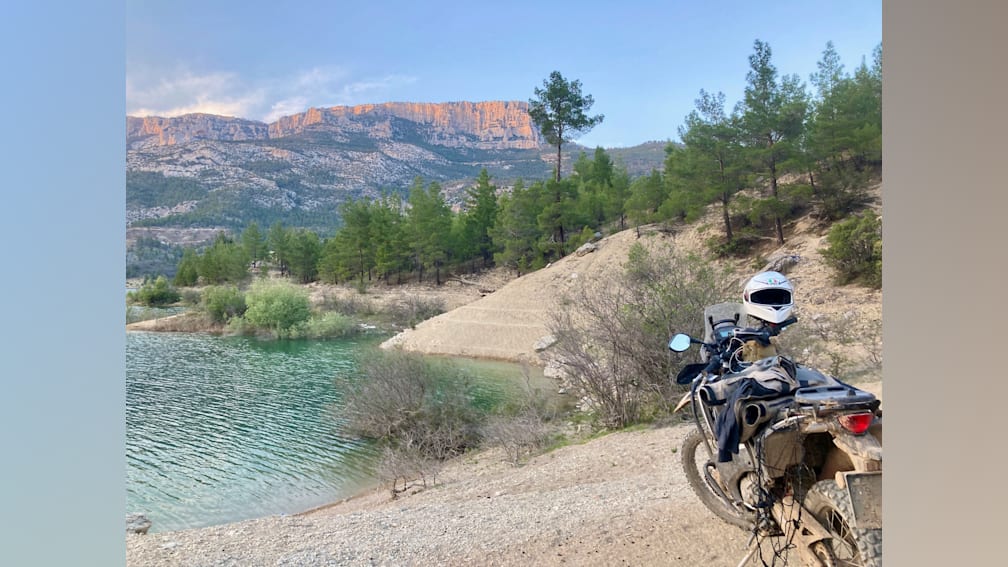 A dirt bike is parked next to a body of water with a mountain in the background.