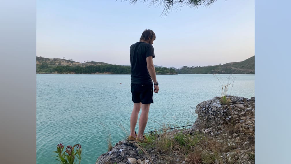 A man standing on rocks next to a body of water with a fish on a hook in his hand.