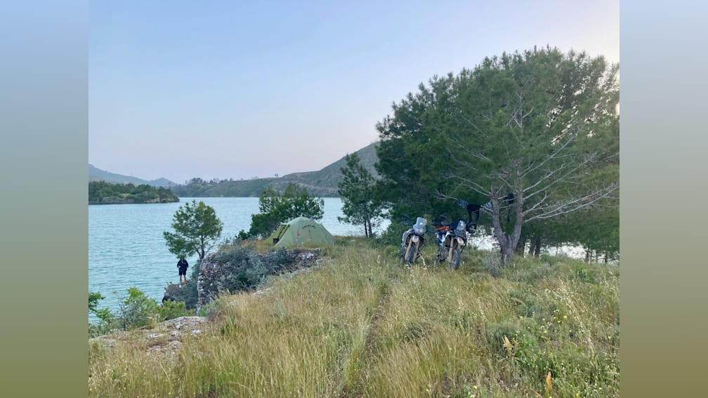 People are camping on a grassy bank overlooking a lake.