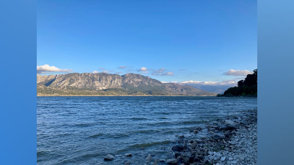 A lake with mountains in the background is calm and still.