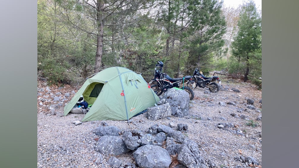 Two motorcycles are parked next to a tent on a rocky campsite.