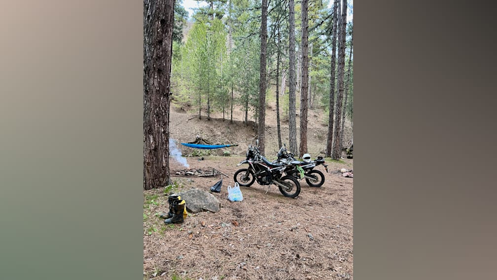 Two motorcycles are parked in a wooded area next to a tent.