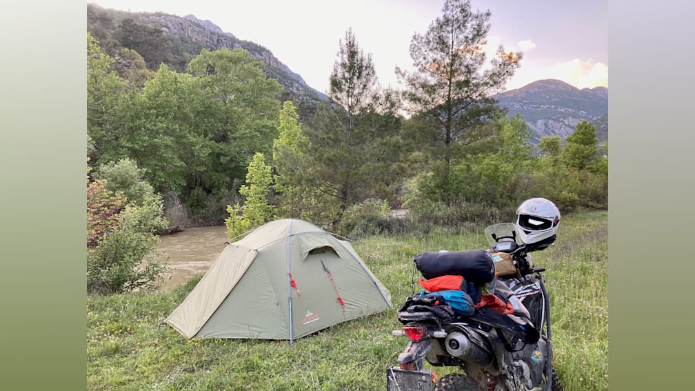 A motorcycle is parked next to a tent on a grassy area by a river.