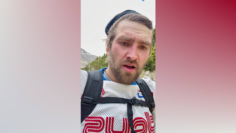 A man with a beard and a white shirt that says 2 on the back is looking at the camera.