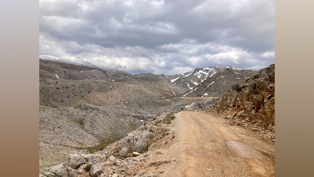 A dirt road winds through a mountain valley with clouds overhead.