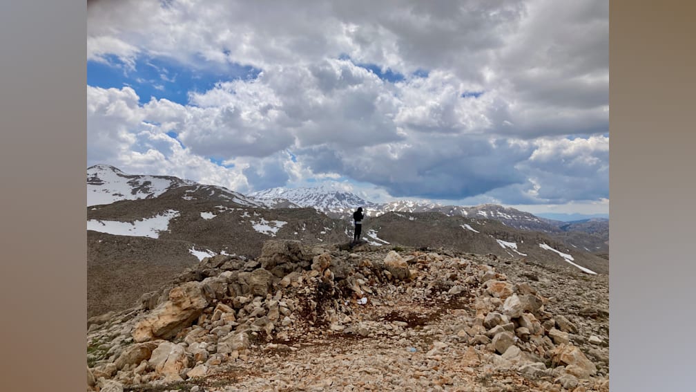 A man stands on a rocky mountain top under a cloudy sky.