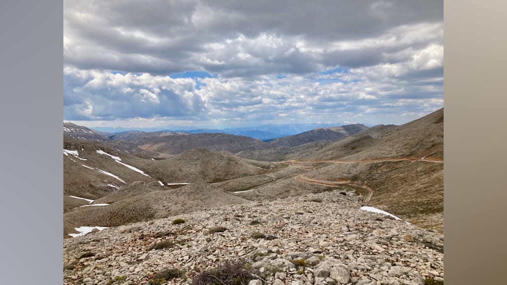 A rocky hillside with a lot of snow on top and a road going through it.