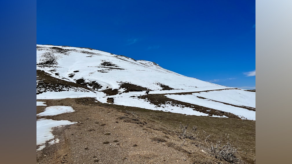 A large body of snow covered ground with a lone hiker in the distance.
