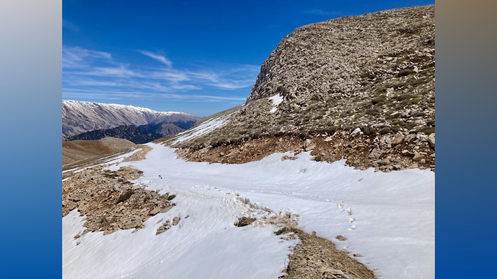 A road covered in snow is shown with mountains in the background.