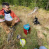 A man with a dog sitting on the grass next to him while he eats from a can.