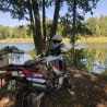 A motorcycle with a helmet on it parked next to a tree by a lake.