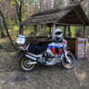 A person wearing a white helmet is sitting on a motorcycle that is parked next to a wooden structure.