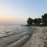 A beach at sunset with the water and sand and a boat in the water.