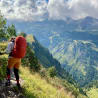 A woman with a red back pack hiking up a mountain with a clear blue sky in the background.