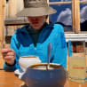A girl in a blue jacket is sitting at a table eating soup with a spoon.