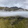 A foggy mountain with rocks on the side and a grassy area in the valley below.