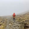 A woman hiking with a red backpack on a rocky mountain.