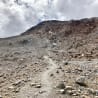 A path goes along a cliff made of boulders and sand.