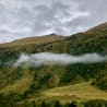 A misty mountain range with trees and grass on the slopes.