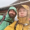 A man and a woman standing together in the rain, the woman is wearing glasses.
