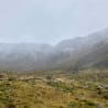 A rocky, grassy field with mountains in the distance.
