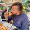 A man with a beard eating pizza in a blue shirt.