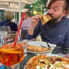 A man with a beard eating pizza and a drink with a straw.