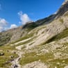 A large mountain with a path going down to the valley with some people walking on the path.