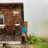 A woman in a blue jacket enters a cabin with wood shingles.
