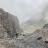 A man with a blue backpack is climbing up a rocky mountain pass.