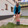 A woman petting her dog while wearing shorts and a blue jacket.