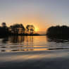The water is calm and the sun is setting behind the trees.