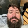 A bearded man is laying in a chair and looking at the camera.
