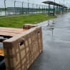 A large wooden bench is strapped to a cardboard box on a wet sidewalk.