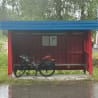 A bicycle is locked onto a red bench on a street and it is raining.
