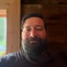 A man with a beard and a brown shirt is smiling.