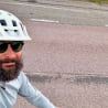 A man with a beard and a white helmet is riding a bike.