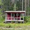 A red cabin in the woods with a green grass area around it.