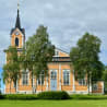 A church with orange and yellow steeples and a green grassy field in the background.