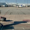 An airport tarmac with a cart in front of a plane with suitcases on it.