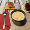 A bowl of soup is sitting on a table next to a spoon and a glass of wine.