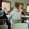 People sitting at a table in a restaurant with a man wearing a sweatshirt that says "present".