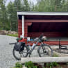 A black bike with a backpack on the back of it parked next to a red shed.