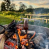 A hot dog on a stick in a fire pit with burning logs.