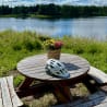 A picnic table with flowers and a helmet on it by the water.