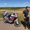 A man standing next to his motorcycle in a field.