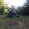 Two people on a motorcycle in the woods, one with a green sock on their left leg.