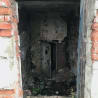A dilapidated room with a broken door and debris on the ground.