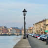 A street lamp on a sidewalk by the water with a bridge in the background.
